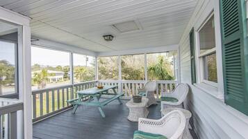 A covered porch with a picnic table and wicker chairs.