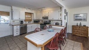 A modern kitchen with white cabinets, a central island, and red chairs. - Beach Blessing- Main (Edisto Island)