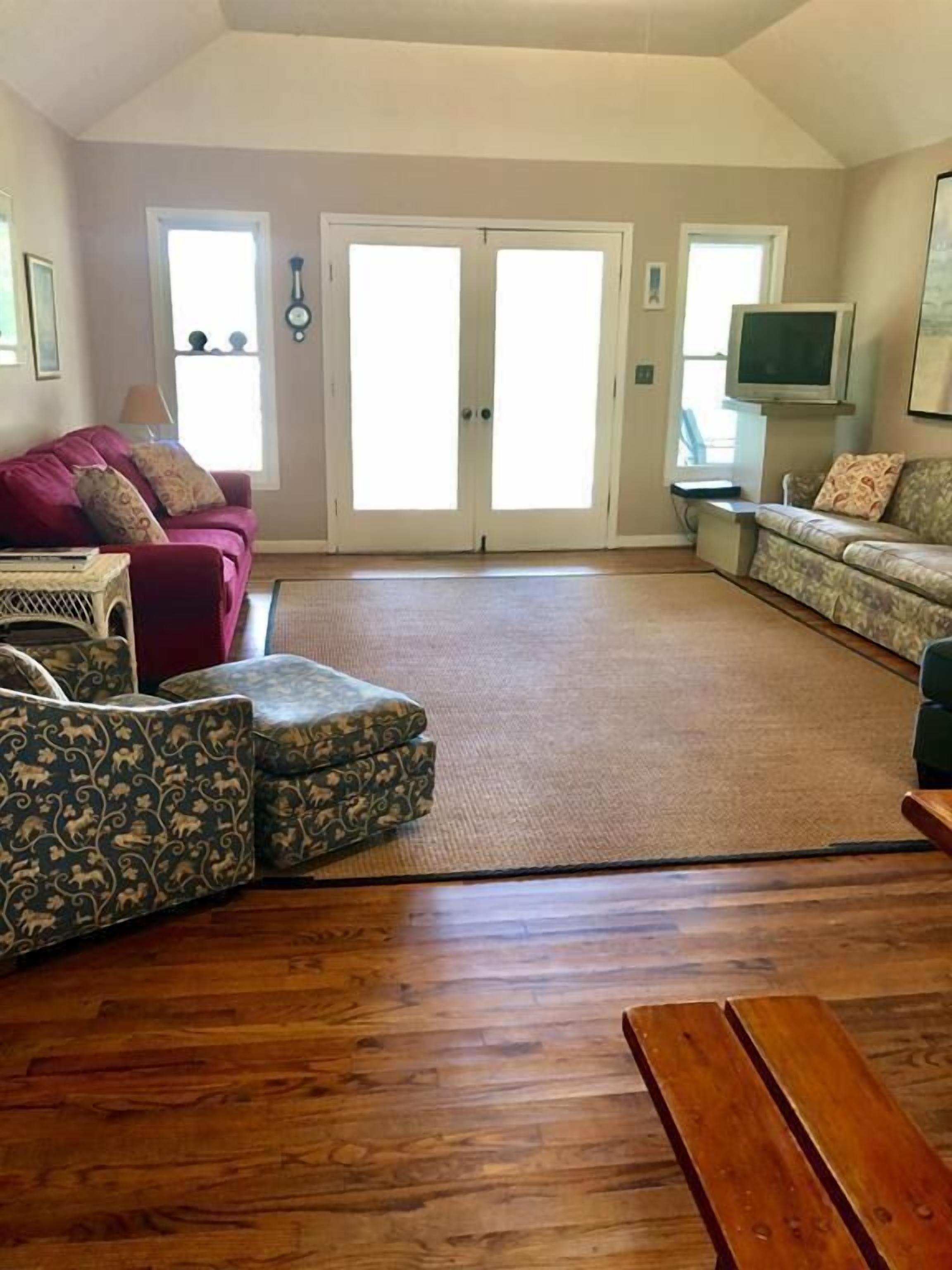 A spacious living room with a high ceiling, a large window, and a sliding glass door leading to a balcony.