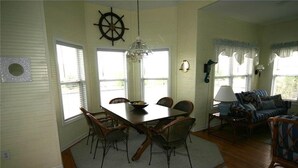 A dining area with a table and chairs, a chandelier, and a view of the outdoors through large windows. - Cupola House (Edisto Island)