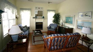 A living room with a sofa, armchair, coffee table, fireplace, and a ceiling fan. - Cupola House (Edisto Island)