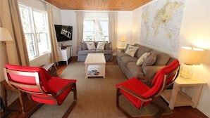 Un salon chaleureux avec un plafond en bois, un canapé gris, deux fauteuils rouges, une table basse et une carte du monde accrochée au mur.