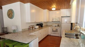 Une cuisine avec des meubles blancs, un plan de travail en granit, un four à micro-ondes, une cuisinière et un évier.