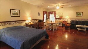 A hotel room with a large bed, a dining table with chairs, a small table with a lamp, and a ceiling fan.