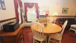 A dining area with a wooden table and white chairs, a sofa, and a small white table with a lamp.