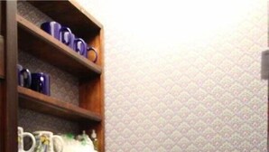 A small kitchenette with a coffee maker, a sink, and a shelf with mugs.