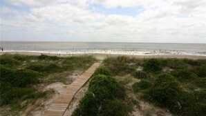 Una playa con un paseo marítimo de madera que lleva a la orilla, rodeada de vegetación.