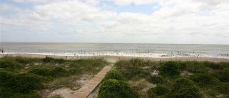 A beach with a wooden boardwalk leading to the shore, surrounded by greenery.