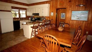 Una cocina con armarios de madera, una mesa de comedor con sillas y un cuadro en la pared.