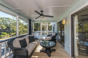 A covered porch with a ceiling fan, wicker furniture, and a glass door leading to a deck.
