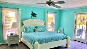 A bedroom with a bed, a ceiling fan, and a door leading to an outdoor area. - Que Sea Ra (Edisto Island)
