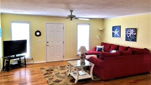 A living room with a red sofa, a television, a ceiling fan, and artwork on the walls. - Que Sea Ra (Edisto Island)