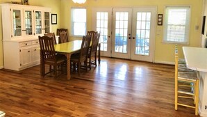 A dining area with a wooden table and chairs, a white cabinet, and a window with blinds. - Que Sea Ra (Edisto Island)
