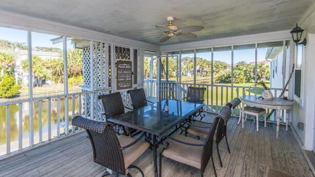 A covered patio with a glass table and chairs, a ceiling fan, and a view of a lake. - Que Sea Ra (Edisto Island)
