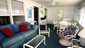 A living room with a blue sofa, a small table, wicker chairs, and a ceiling fan. - Rich Tymes (Edisto Island)