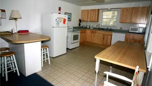 A compact kitchen with wooden cabinets, a refrigerator, a microwave, and a small dining area with stools. - Rich Tymes (Edisto Island)