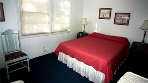 A bedroom with a bed, a chair, a lamp, and two framed pictures on the wall. - Rich Tymes (Edisto Island)
