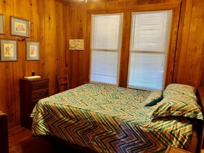 A wooden-paneled room with a bed, a nightstand, and framed pictures on the wall. - Salley/morrison (Edisto Island)