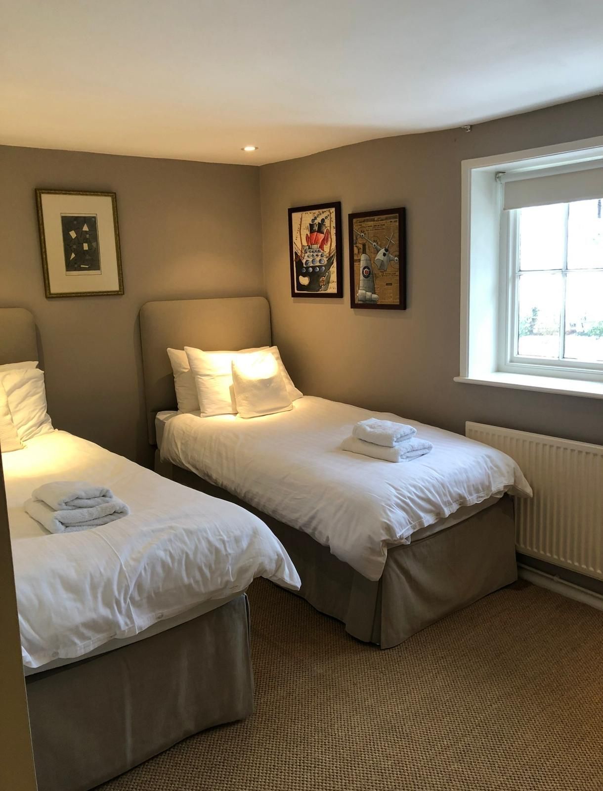 A hotel room with two single beds, a window with a view, and framed artwork on the walls.