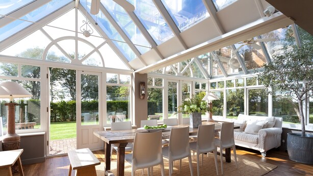 A conservatory with a wooden table, white chairs, and a sofa.
