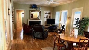 A spacious living area with a wooden floor, a dining table with chairs, a sofa, a TV, and a fireplace. - Seaczar's Retreat (Edisto Island)