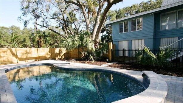 A swimming pool with a curved edge, surrounded by a wooden fence and a brick border. - Seaczar's Retreat (Edisto Island)