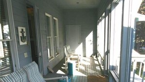A covered porch with striped chairs, a small table, and a view of the outside. - Seaczar's Retreat (Edisto Island)