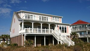 A two-story beachfront house with a balcony and a staircase leading to the upper floor.