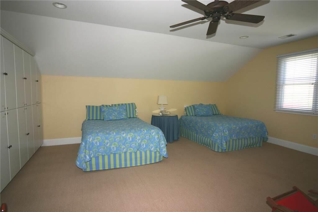 A bedroom with two beds, a ceiling fan, a window with blinds, and a wardrobe.