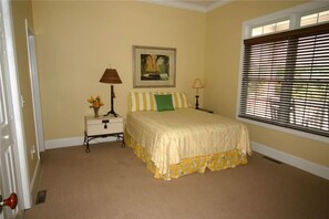 A bedroom with a bed, a nightstand, a lamp, a picture on the wall, and a window with blinds.