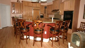 A kitchen with wooden cabinets, a central island with bar stools, a vintage radio, and a chandelier.