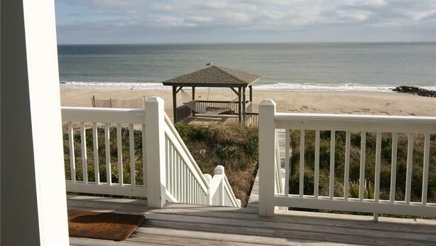 A beach view from a wooden deck with a gazebo in the middle.