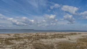 Ein Strand mit Sand und vereinzelter Vegetation unter einem teilweise bewölkten Himmel.