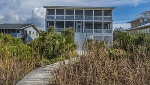 Ein Strandhaus mit zwei Etagen, einer überdachten Veranda und einem Weg zum Eingang.