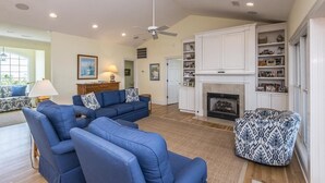Ein geräumiges Wohnzimmer mit Kamin, blauen Sofas und einem gemusterten Pouf.