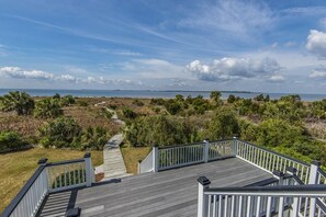 A wooden deck with white railings overlooking a coastal landscape with a clear sky. - The Pearl (Edisto Island)