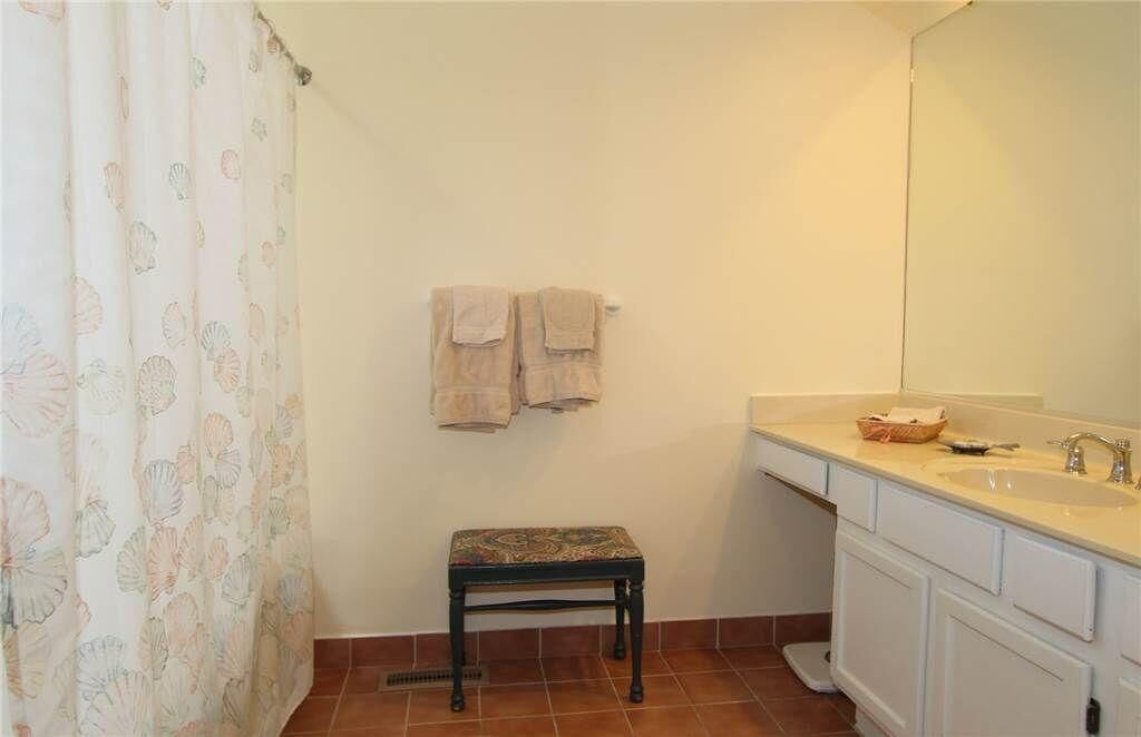 A bathroom with a shower curtain, a bench, a sink, and towels hanging on the wall.