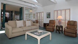 A living room with a beige sofa, two brown leather armchairs, a glass coffee table, and a lamp on a side table. - The Point (Edisto Island)