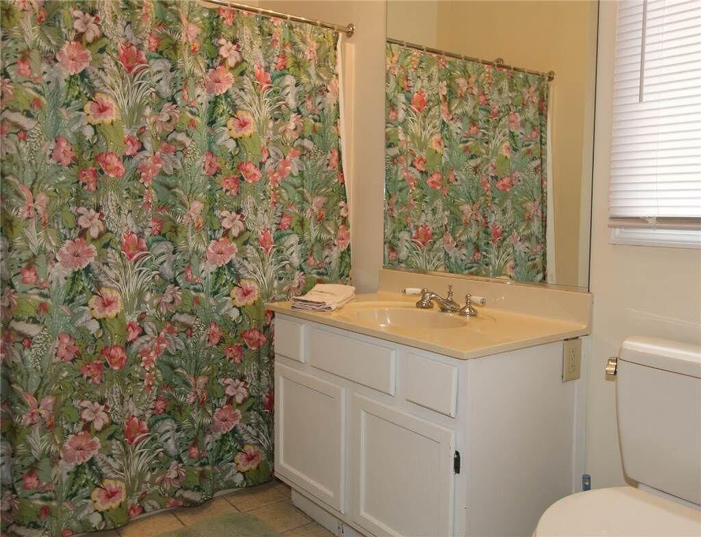 Un baño con cortina de ducha estampada con flores, un lavabo con espejo y un inodoro.