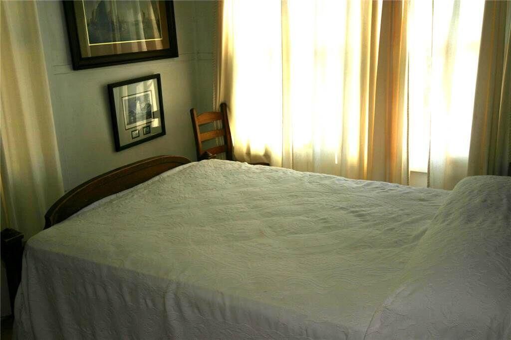 Ein Schlafzimmer mit einem großen Bett, einem Holzstuhl und zwei gerahmten Bildern an der Wand.