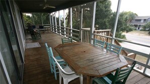 Eine überdachte Veranda mit Holztisch und -stühlen, einem Geländer und Blick auf die Straße und die grüne Umgebung.