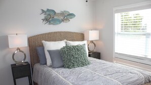 A neatly arranged bedroom with a large bed, two bedside tables with lamps, a decorative wall piece, and a window with blinds.