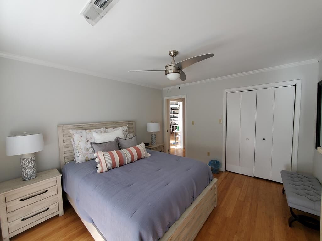 Une chambre à coucher comprenant un lit, des tables de chevet, un banc, un ventilateur de plafond et une armoire.