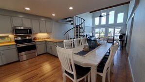 A modern kitchen with white cabinets, stainless steel appliances, and a wooden dining table with white chairs.