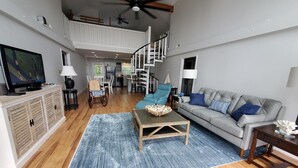 A spacious living room with a high ceiling, a staircase, a television, and a dining area.
