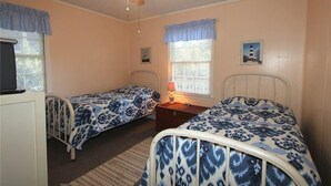 A bedroom with two single beds, a ceiling fan, a nightstand with a lamp, and a dresser. - Creamsicle (Edisto Island)