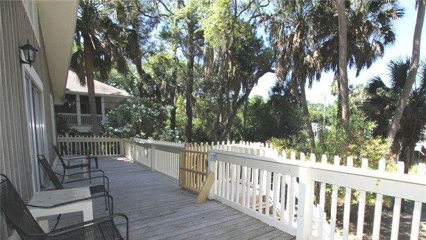 A wooden deck with outdoor seating, a white fence, and a view of trees and a building.