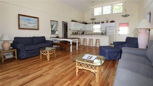 A spacious living room with a wooden floor, a sofa, a coffee table, and a dining area with stools.