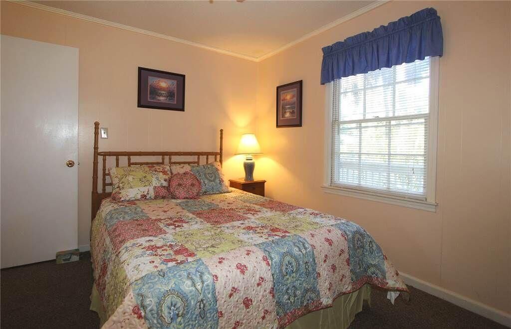 A bedroom with a bed, a nightstand, a lamp, a window with blinds, and two framed pictures on the wall.