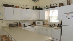 A kitchen with white cabinets, a microwave, a refrigerator, and wooden stools.